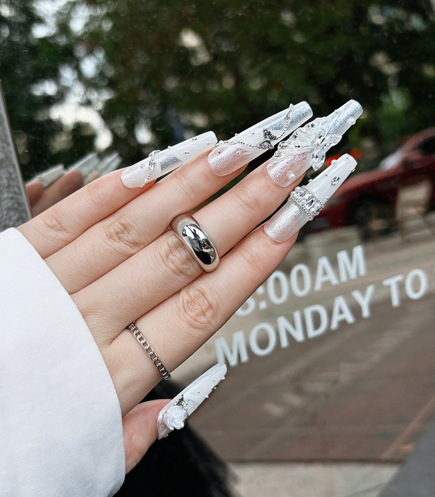 Hand with white acrylic nails and silver decorations against a blurred background