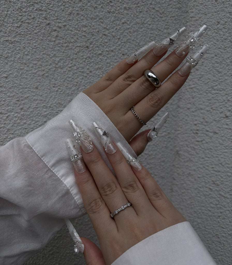 Close-up of hands with decorative nails and rings against a neutral background