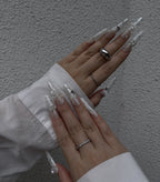 Close-up of hands with decorative nails and rings against a neutral background