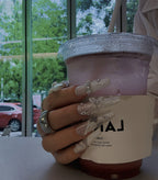 Hand holding a pink drink with a straw, blurred outdoor background