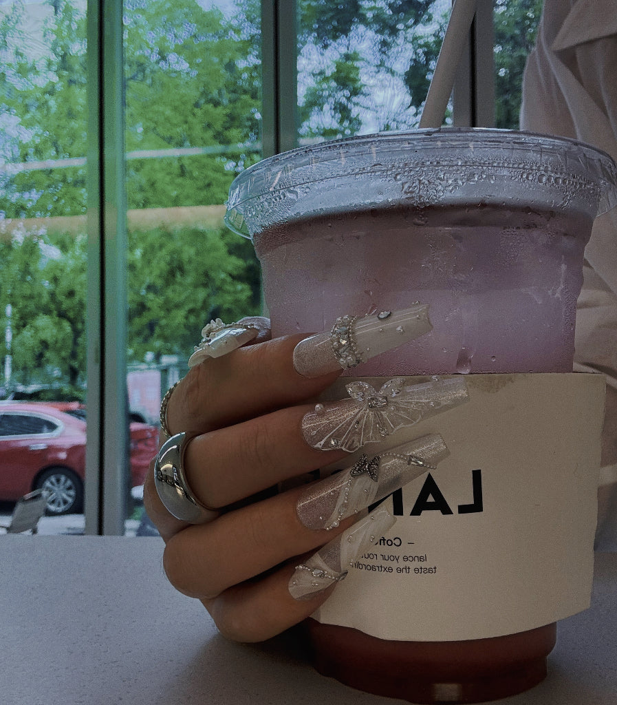 Hand holding a pink drink with a straw, blurred outdoor background