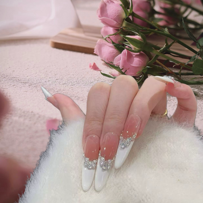 Close-up of a hand with long, white nails featuring silver glittery accents, holding pink flowers.