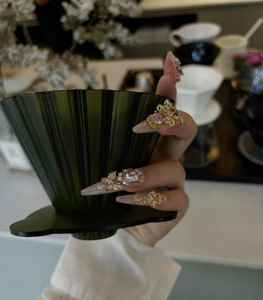 Hand holding a black teacup with decorative rings on fingers in a kitchen setting