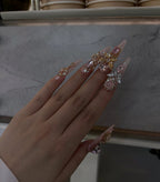 Hand with long, decorated nails holding a small decorative item against a neutral background