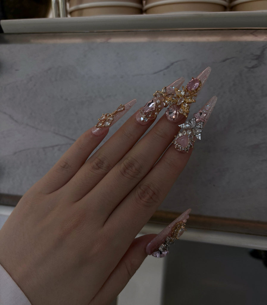 Hand with long, decorated nails holding a small decorative item against a neutral background