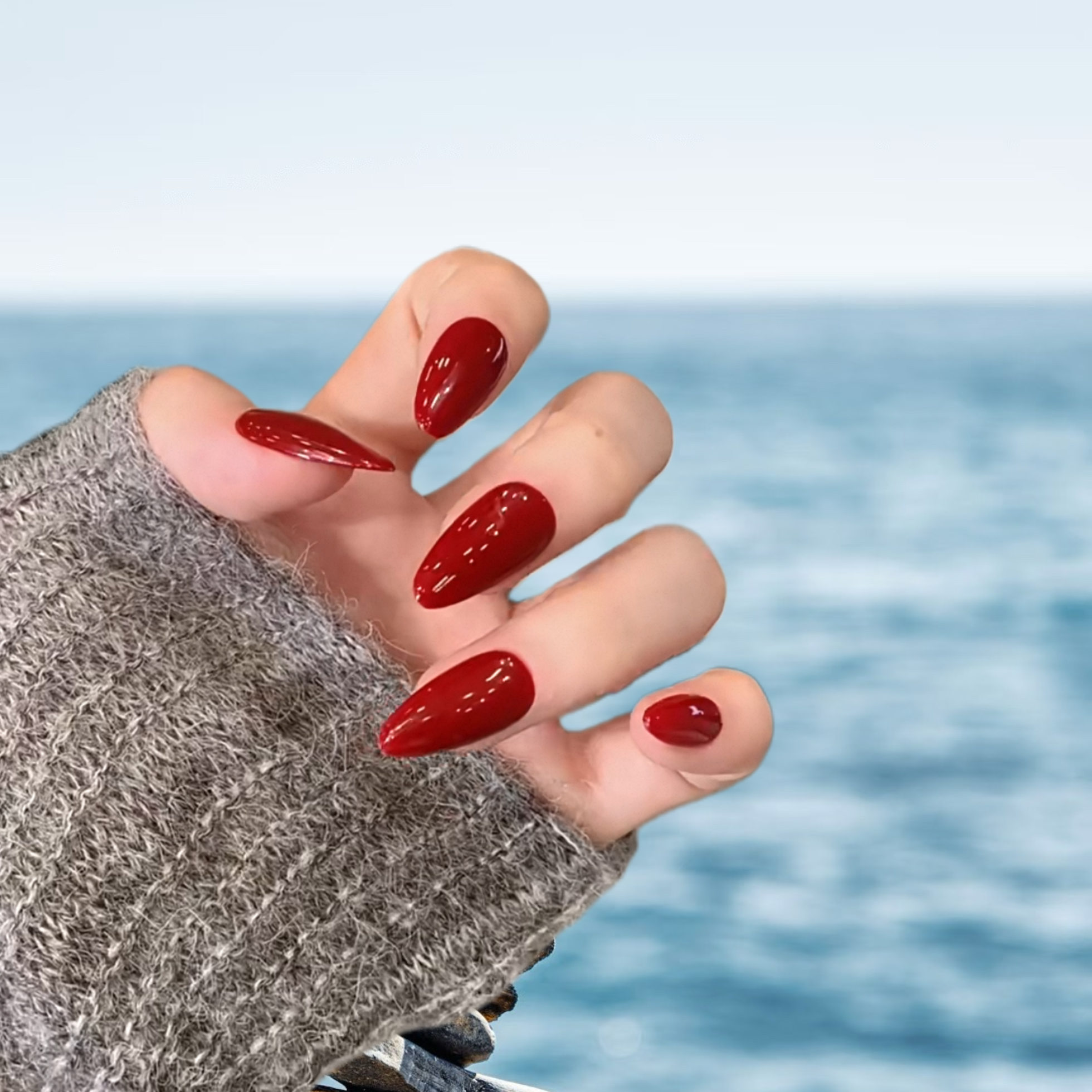 Hand with red nail polish against a blurred ocean background