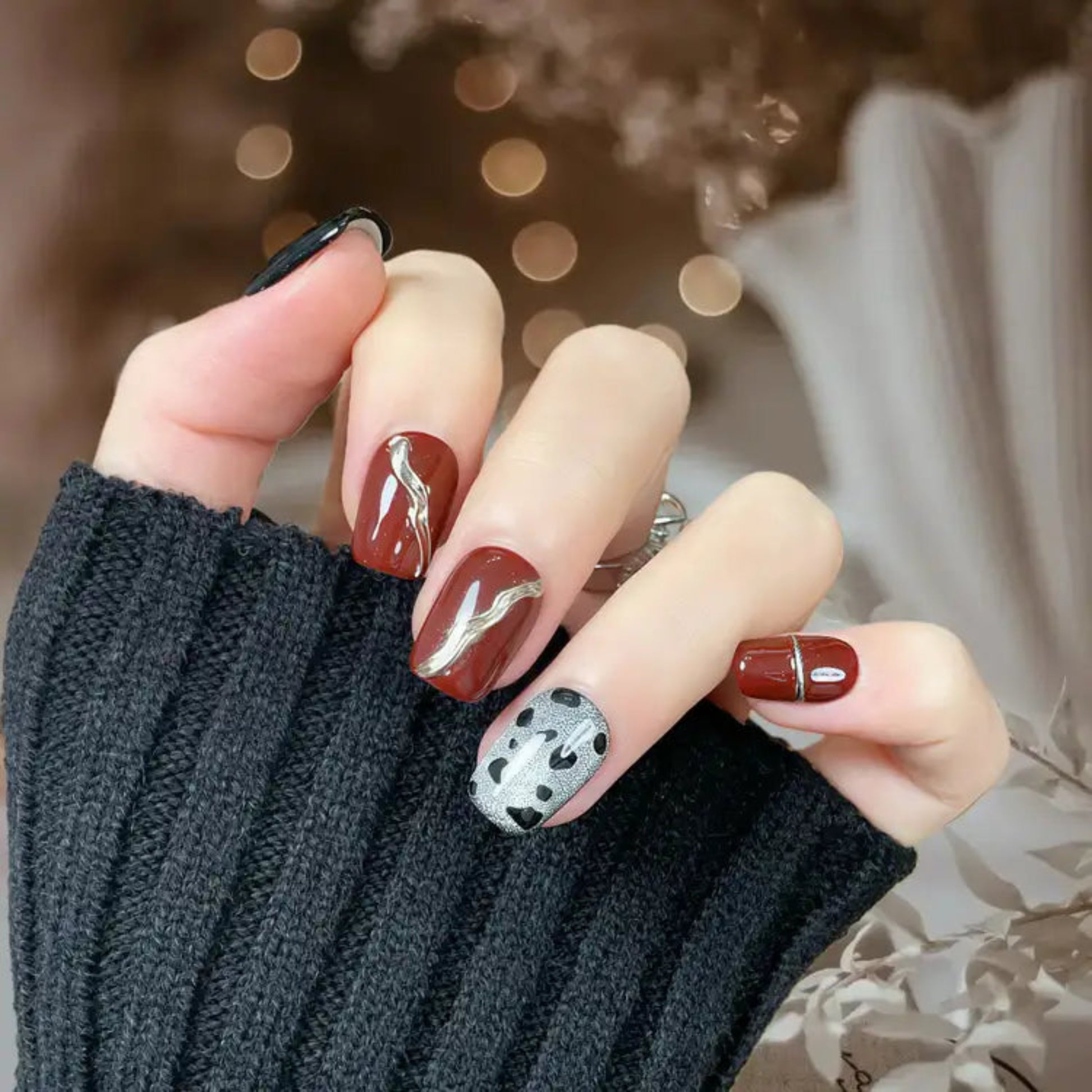 Close-up of a hand with stylish nail art wearing a dark sweater.