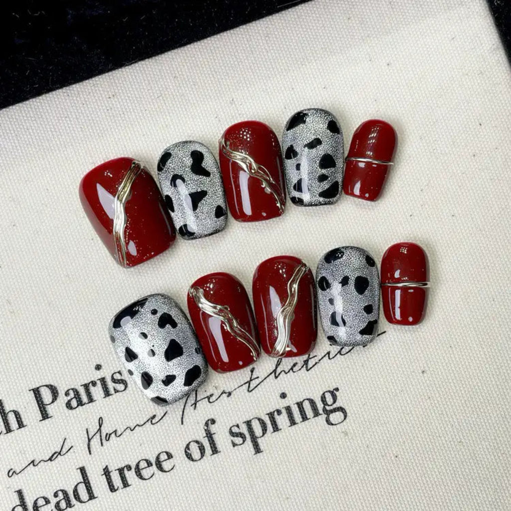 Nails with red and black designs on a white surface with text