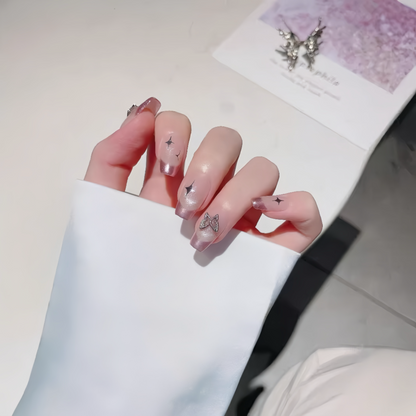 Hand with pink nail polish and butterfly designs, wearing a white sleeve, on a light background.