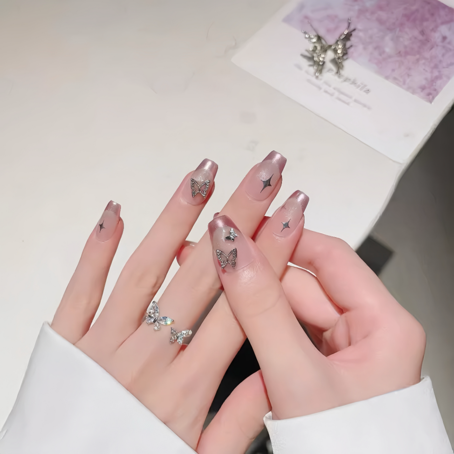 Close-up of hands with decorative nail art featuring butterflies and stars, wearing a white sleeve.