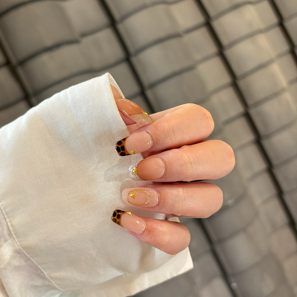 Close-up of a hand with gold nail art on a neutral background