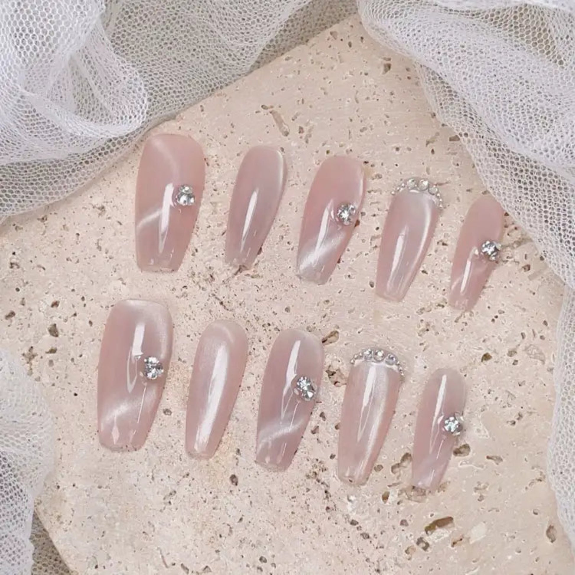 Set of pink press-on nails with rhinestones on a textured surface