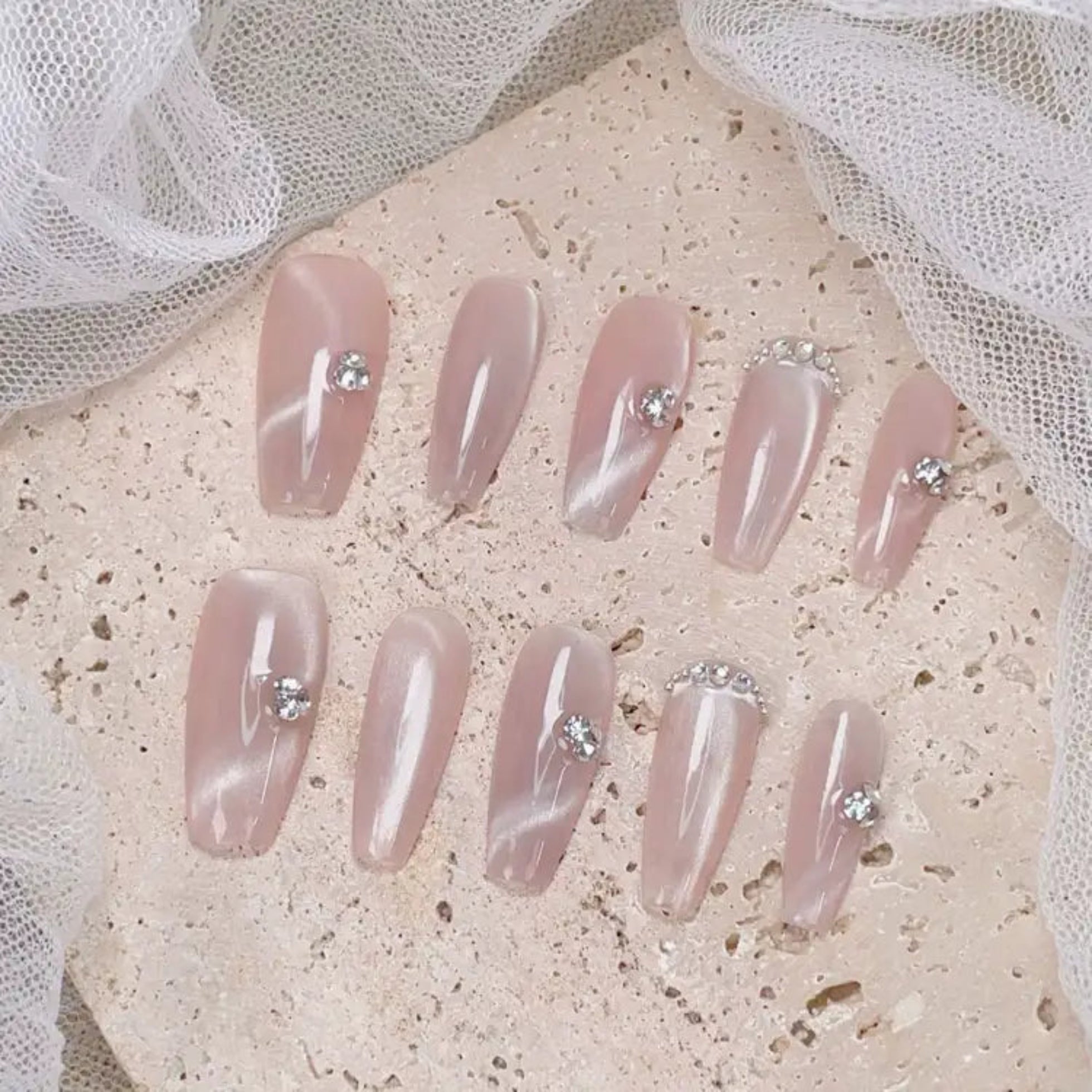 Set of pink press-on nails with rhinestones on a textured surface