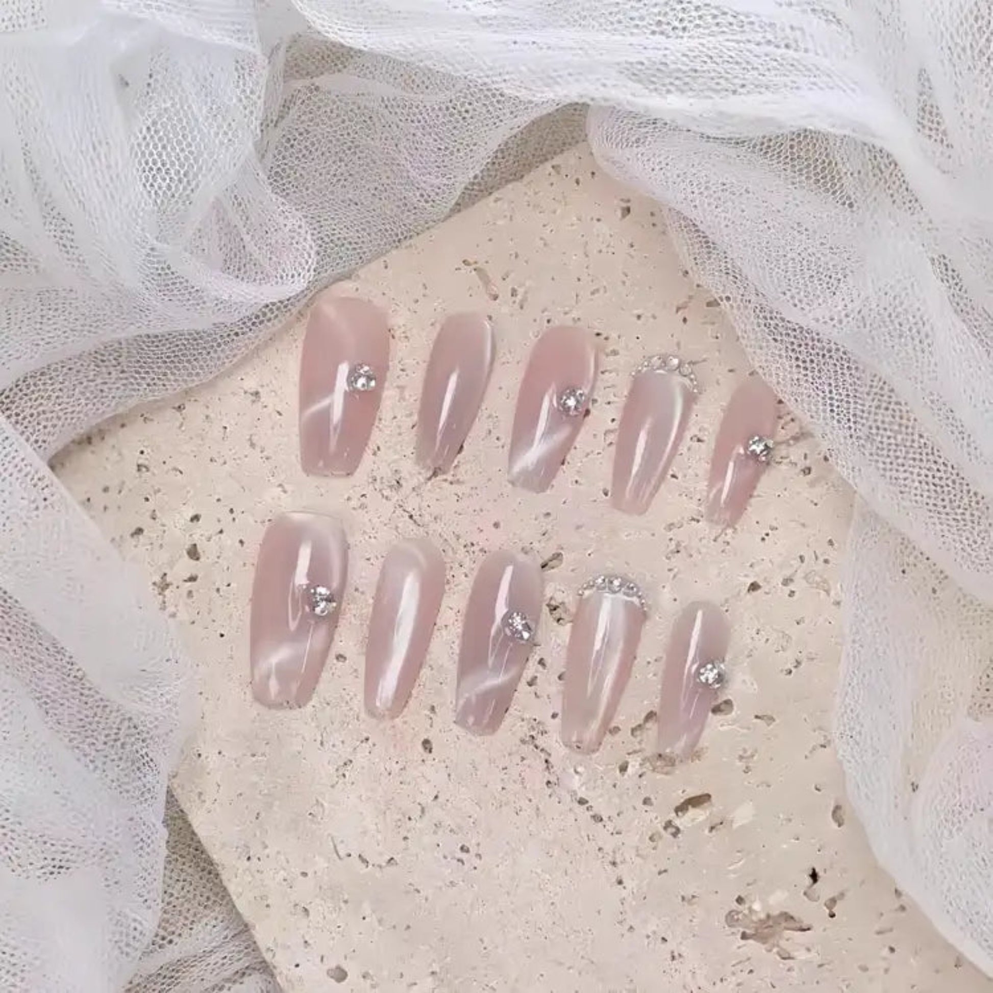 Set of pink press-on nails with rhinestones on a textured surface