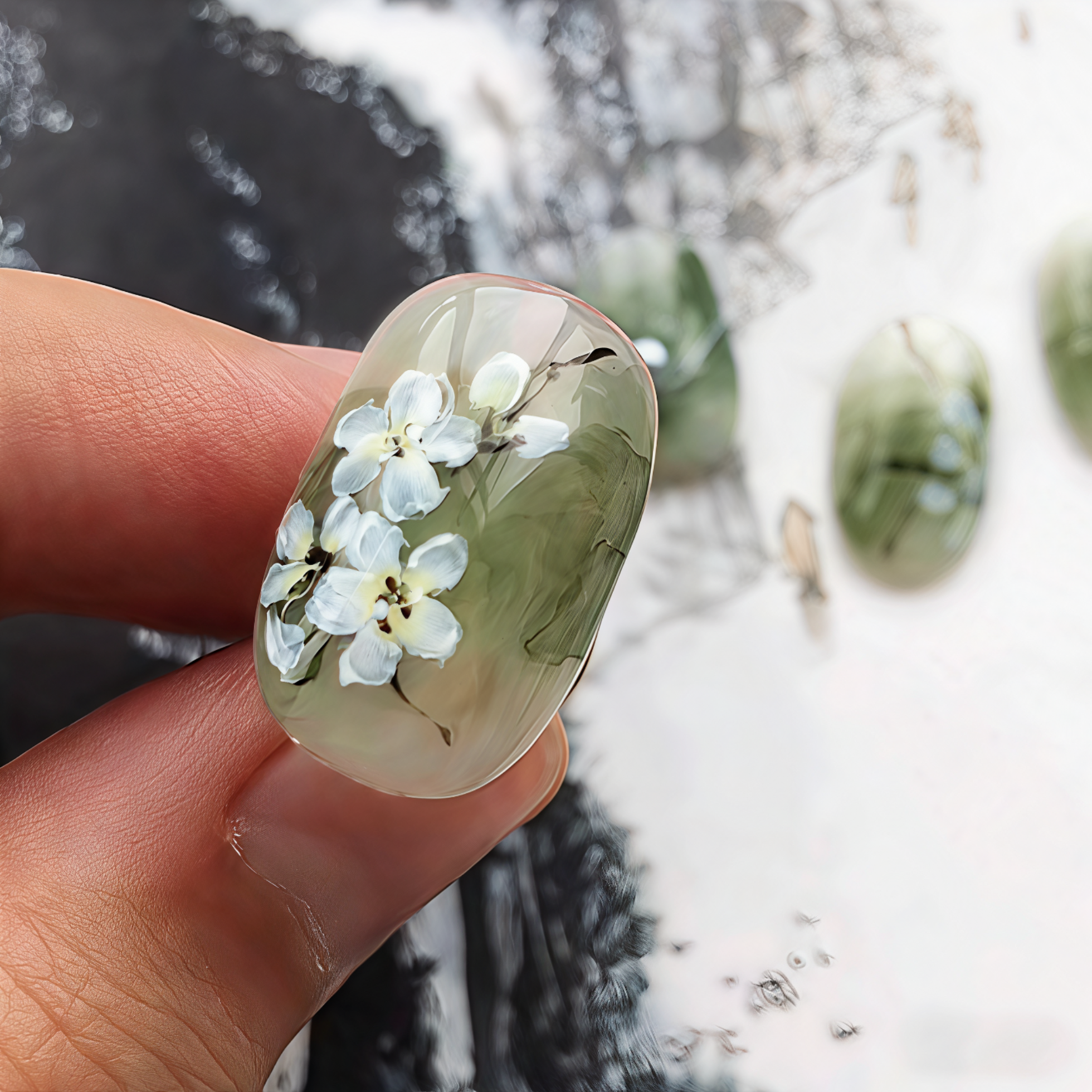 Nail with floral design held by a hand against a blurred natural background