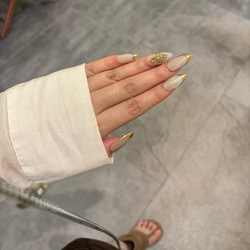 Hand with beige and gold nail polish on a neutral background