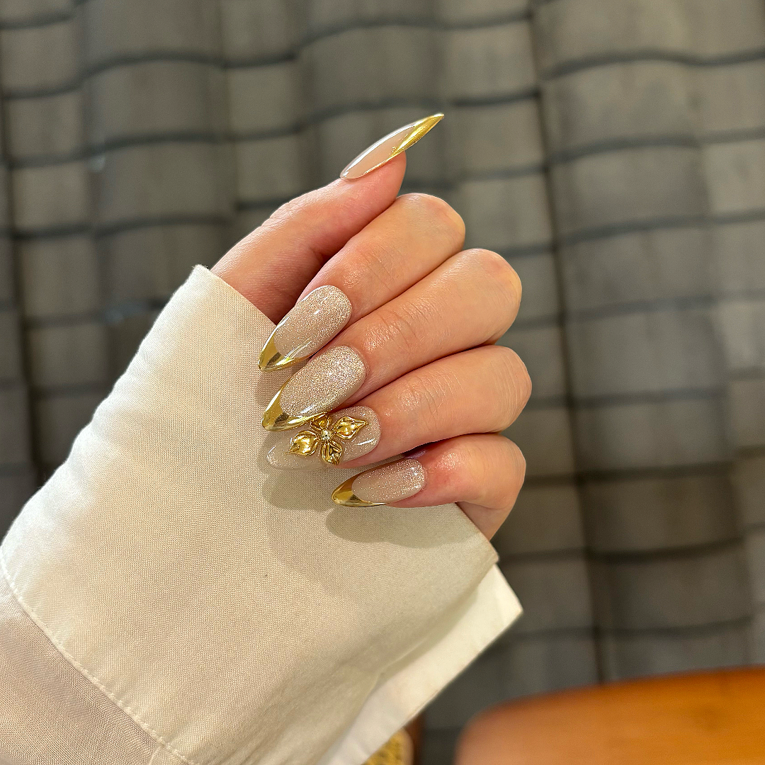 Hand with glittery nails and gold accents against a plaid background