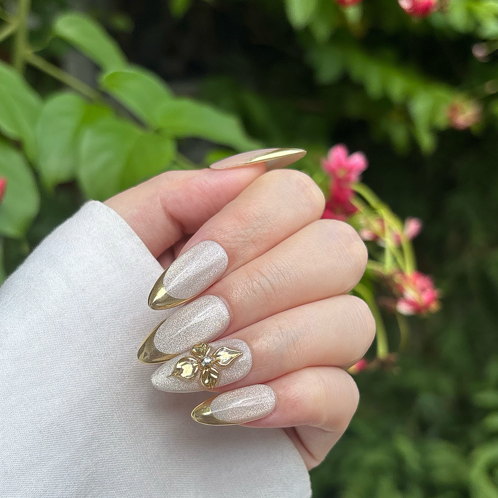 Hand with decorative nails holding a white flower against a blurred green background