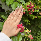 Hand with painted nails holding pink flowers against a green leafy background