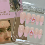 Set of pink and white flower-themed false nails in a clear case with a magazine in the background.
