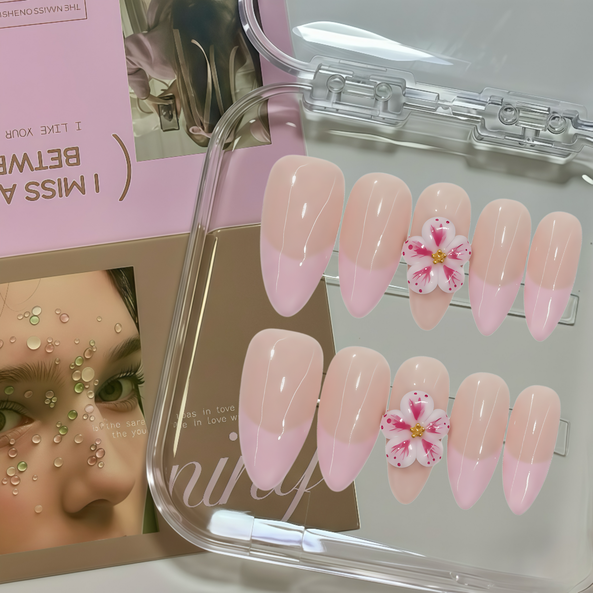 Set of pink and white flower-themed false nails in a clear case with a magazine in the background.