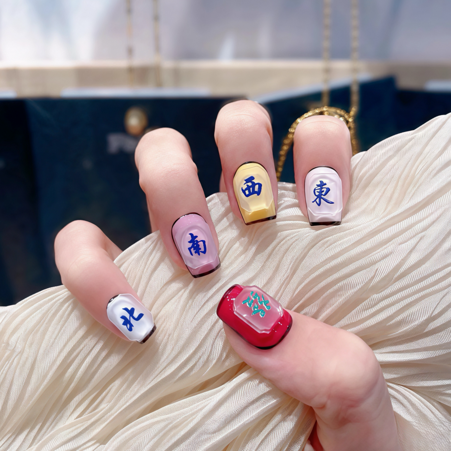 Nails with colorful designs and text held by a hand against a blurred background