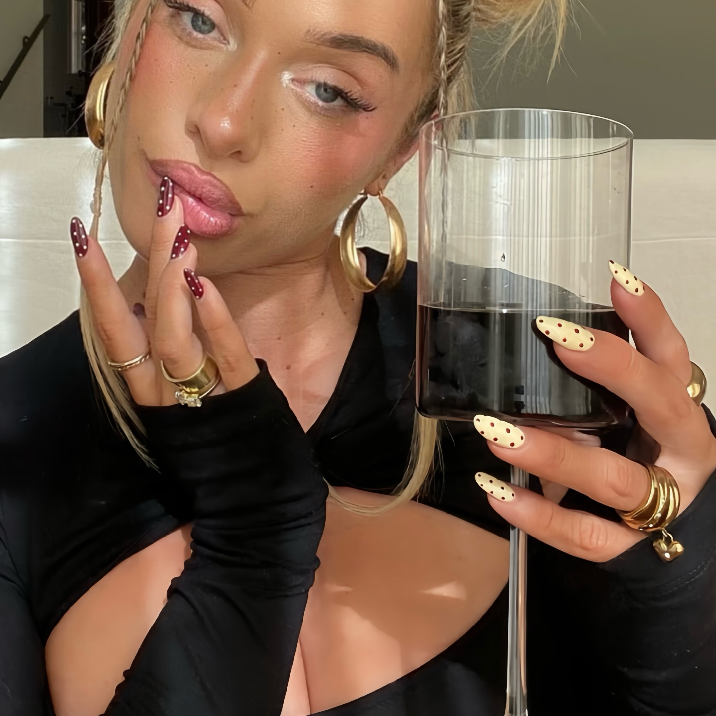 Woman holding a glass of red wine with stylish nail polish and jewelry.