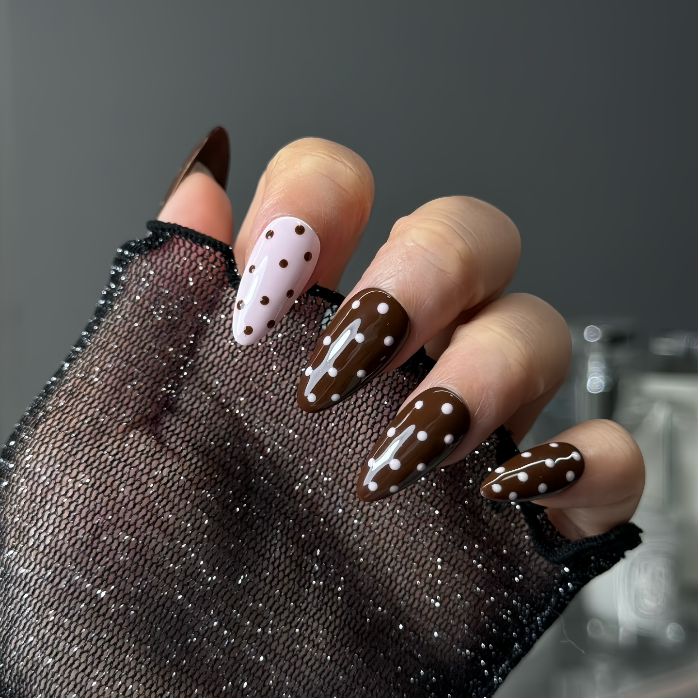 Hand with decorative nails wearing a black glove on a neutral background