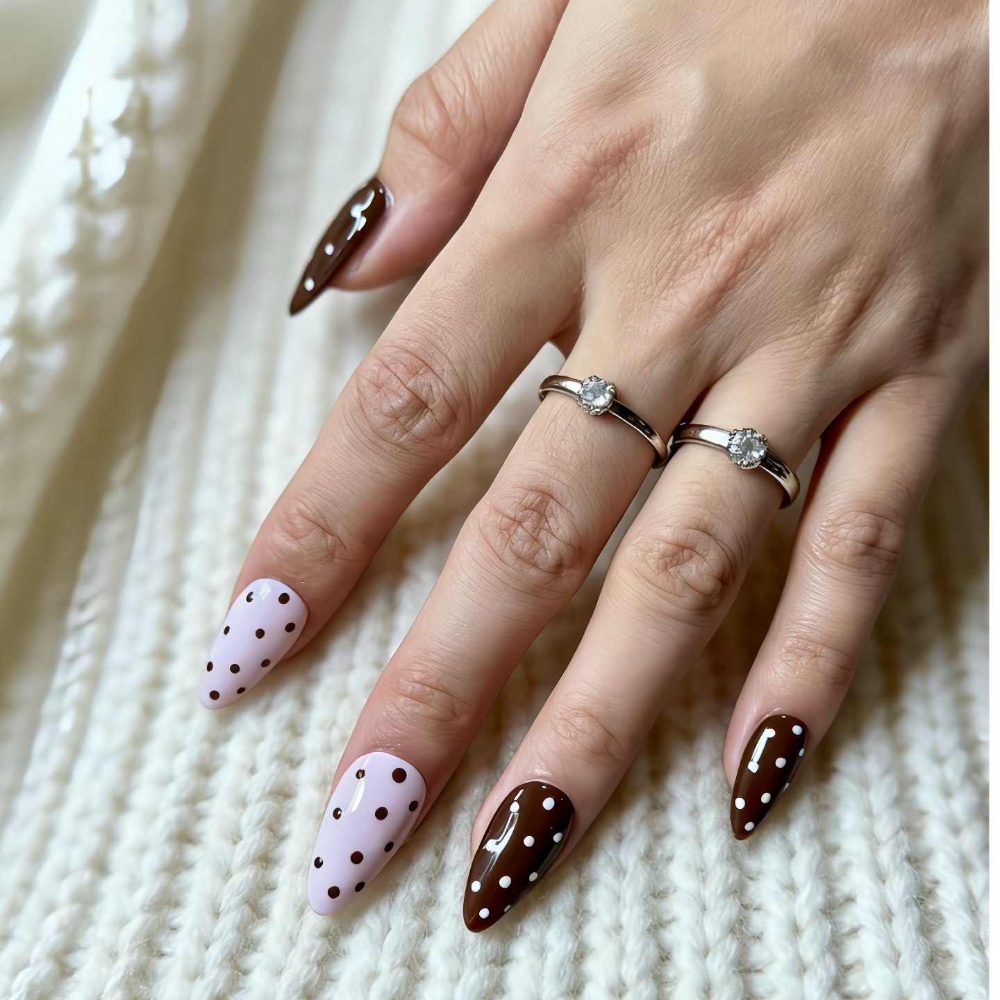 Hand with brown and white polka dot nail design on a textured white background