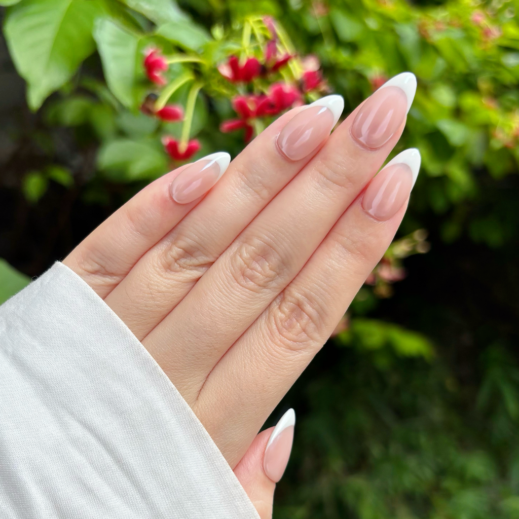 Hand with light pink nail polish against a blurred green and red floral background