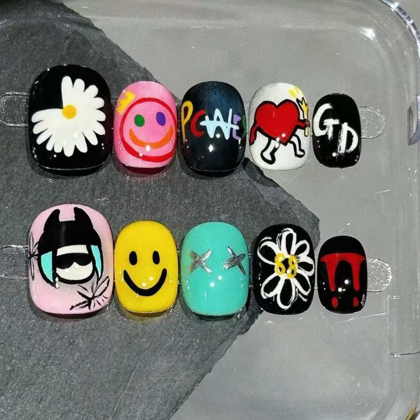 Colorful nail art designs on a clear tray with various patterns and symbols.