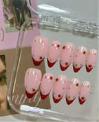 Set of pink and red gradient nail designs with floral decorations in a clear case.