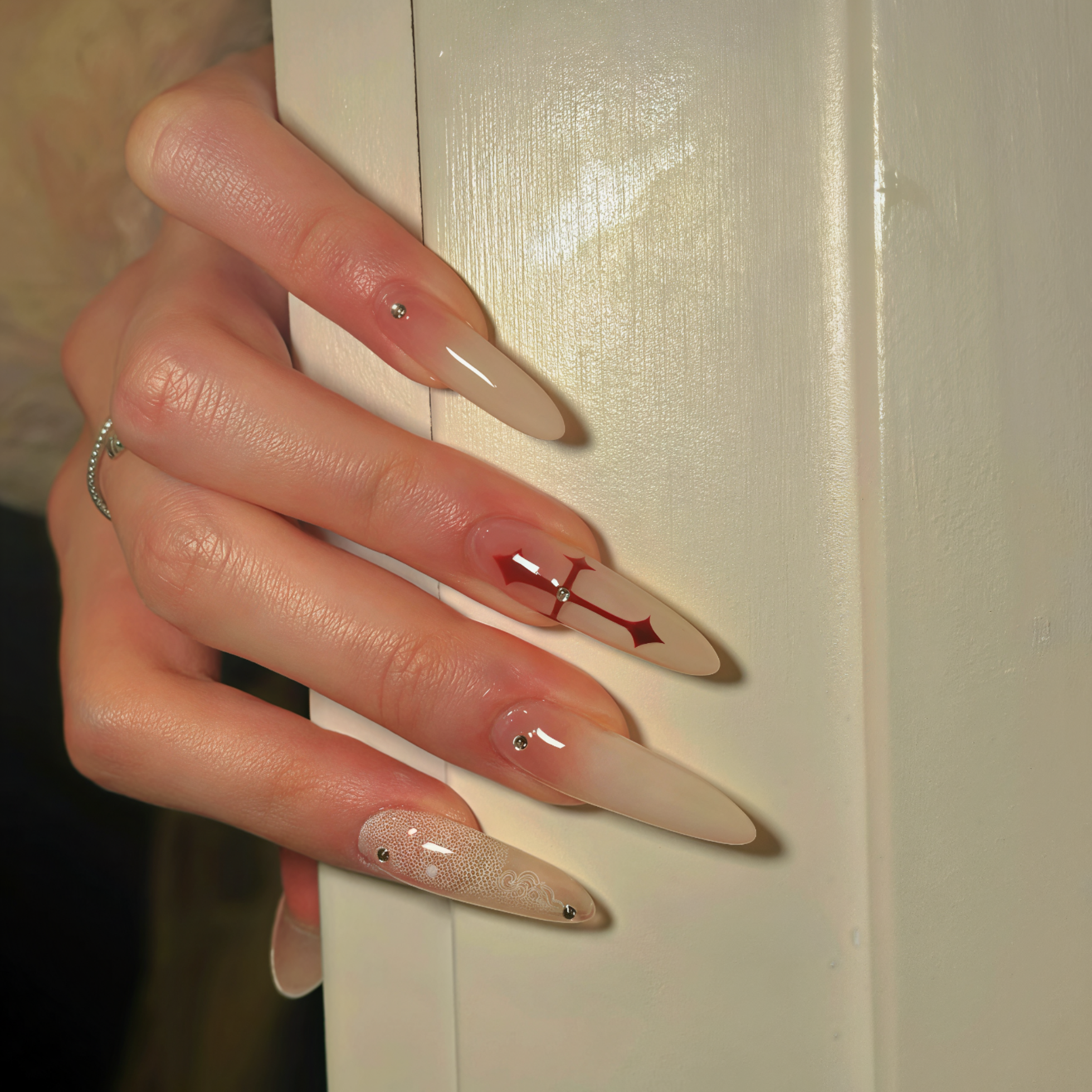 Close-up of a hand with long, pointed nails featuring red and clear design against a neutral background.