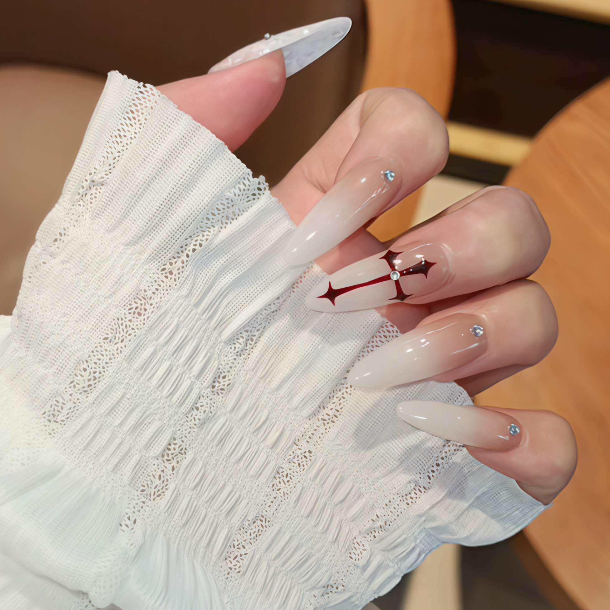 Close-up of a hand with long, almond-shaped nails featuring red anchor design and rhinestones.