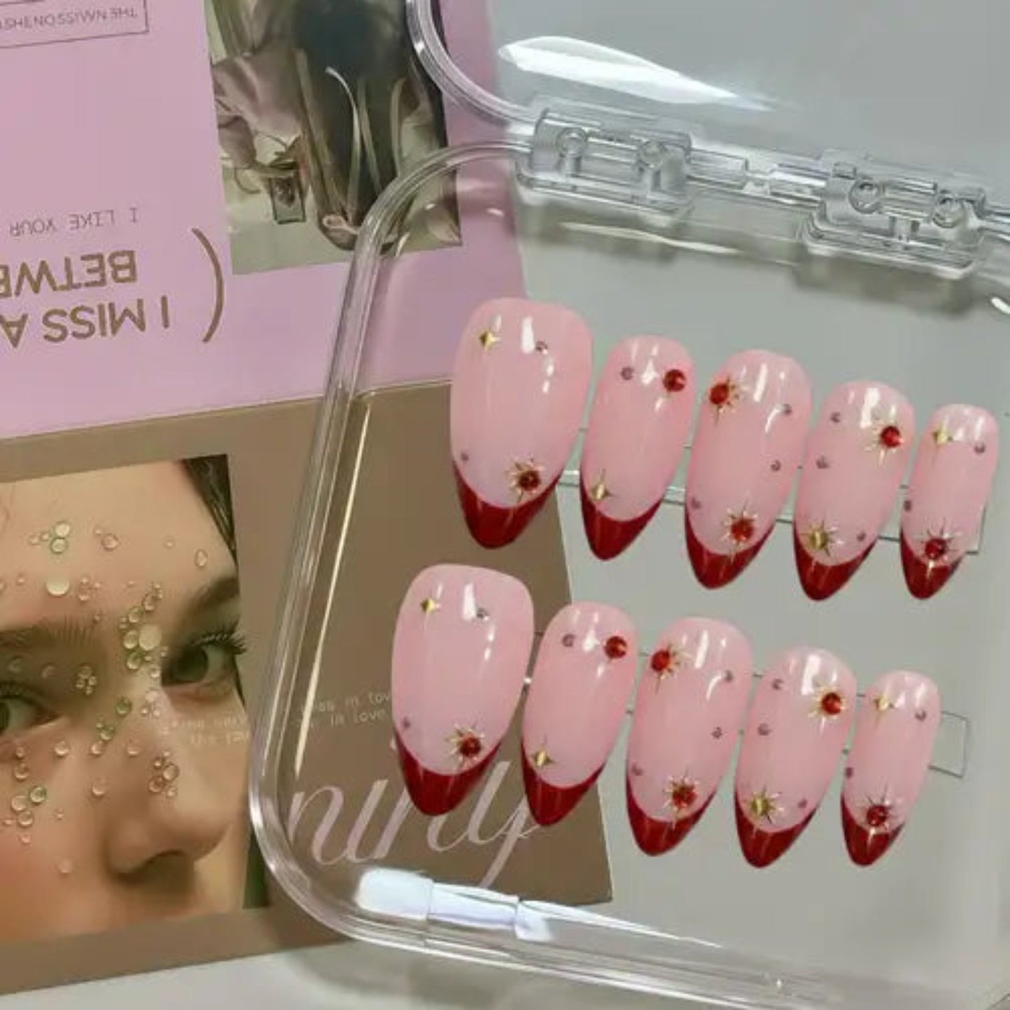 Set of pink and red gradient nail designs with floral decorations in a clear case.