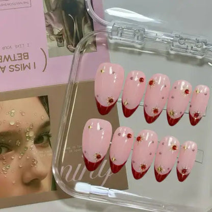 Set of pink and red gradient nail designs with floral decorations in a clear case.