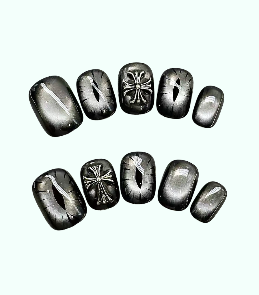 A set of ten black cat-eye press-on nails arranged in two rows against a pale mint green background. The set includes various designs such as solid black, striped patterns, and raised metallic silver cross and floral motifs.