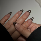 Close-up of a hand with beige nail polish and decorative black and gold nail tips.