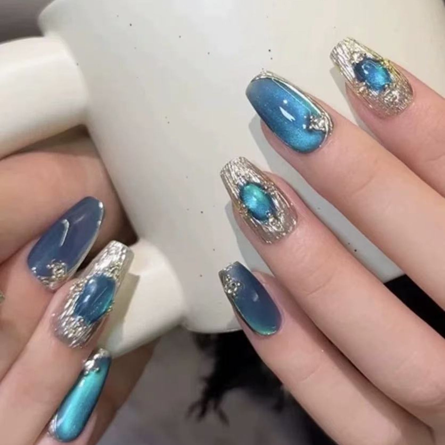Hand with blue and silver nail design holding a white mug.