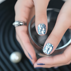 Close-up of a hand with glittery nail polish holding a pearl.