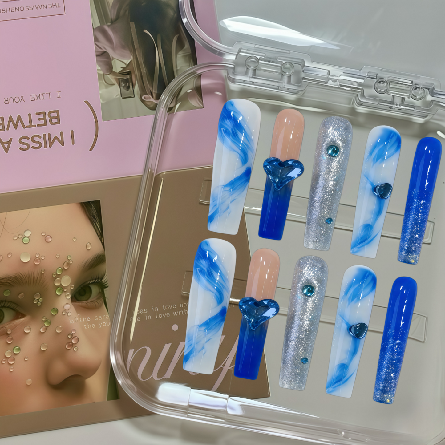 Set of blue, white, and clear nail art designs in a clear case with a magazine in the background.
