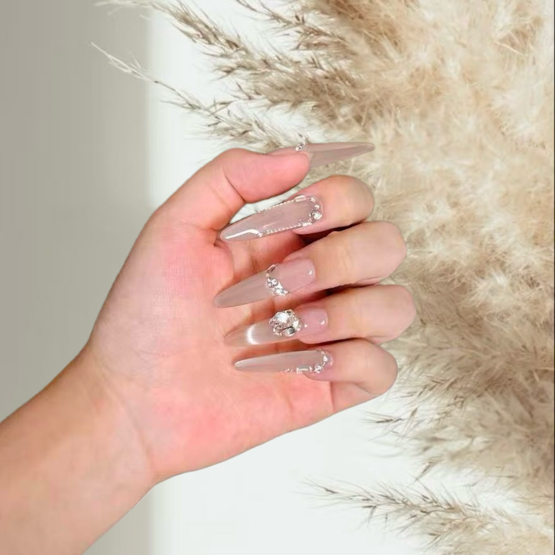 Hand with clear acrylic nails featuring rhinestones against a soft background