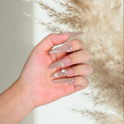 Hand with clear acrylic nails featuring rhinestones against a soft background