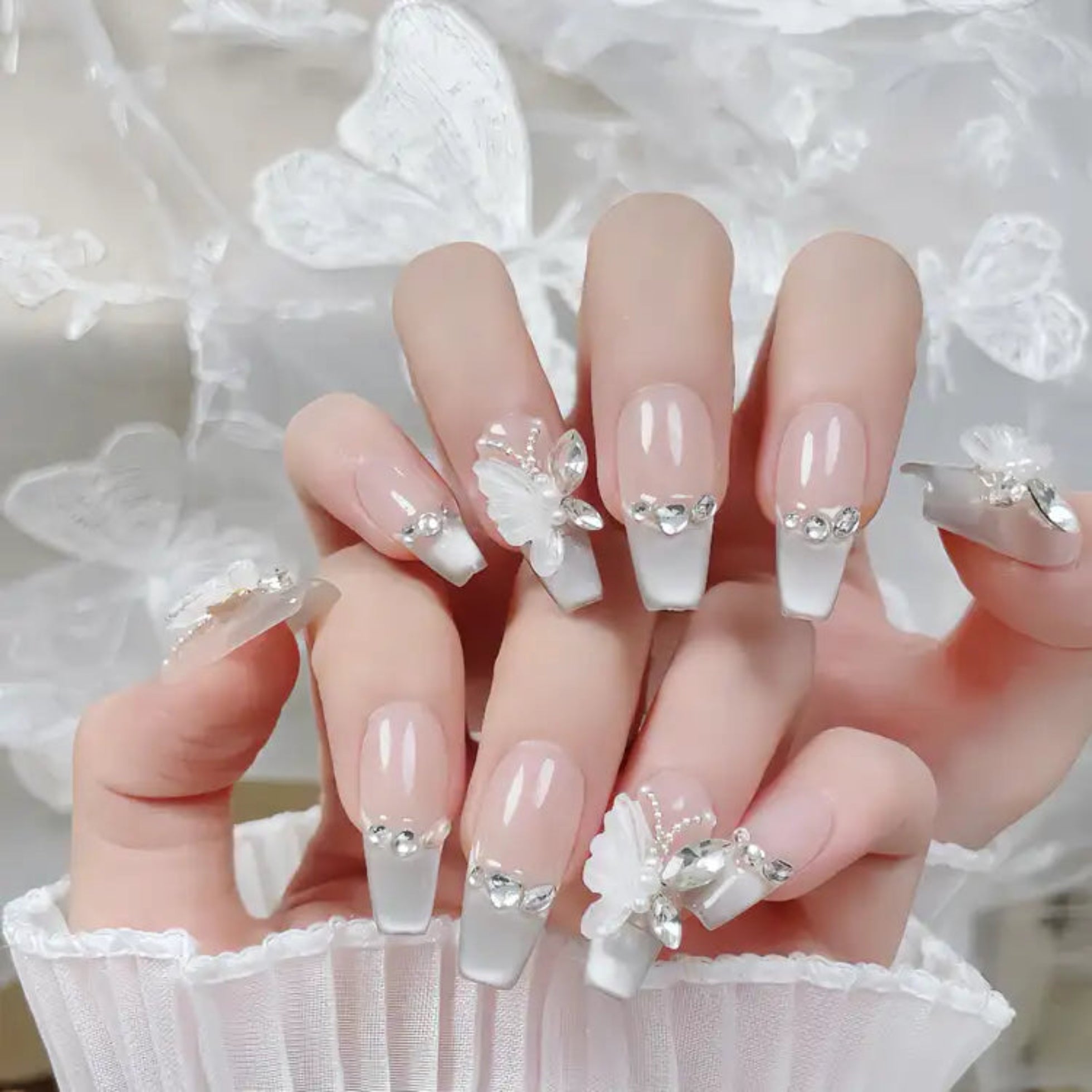 Nails with floral and crystal decorations held by a person wearing a white lace garment.
