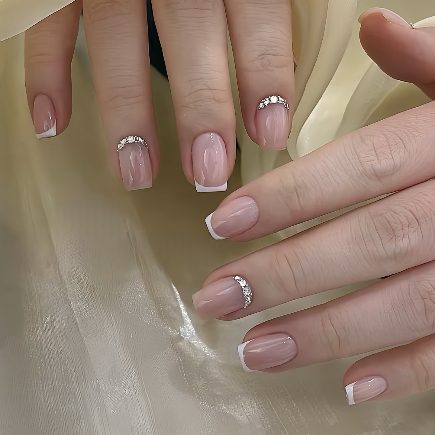 Close-up of hands with pink nail polish and diamond nail rings on a beige fabric background