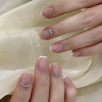 Close-up of hands with pink nail polish and decorative elements on a light fabric background