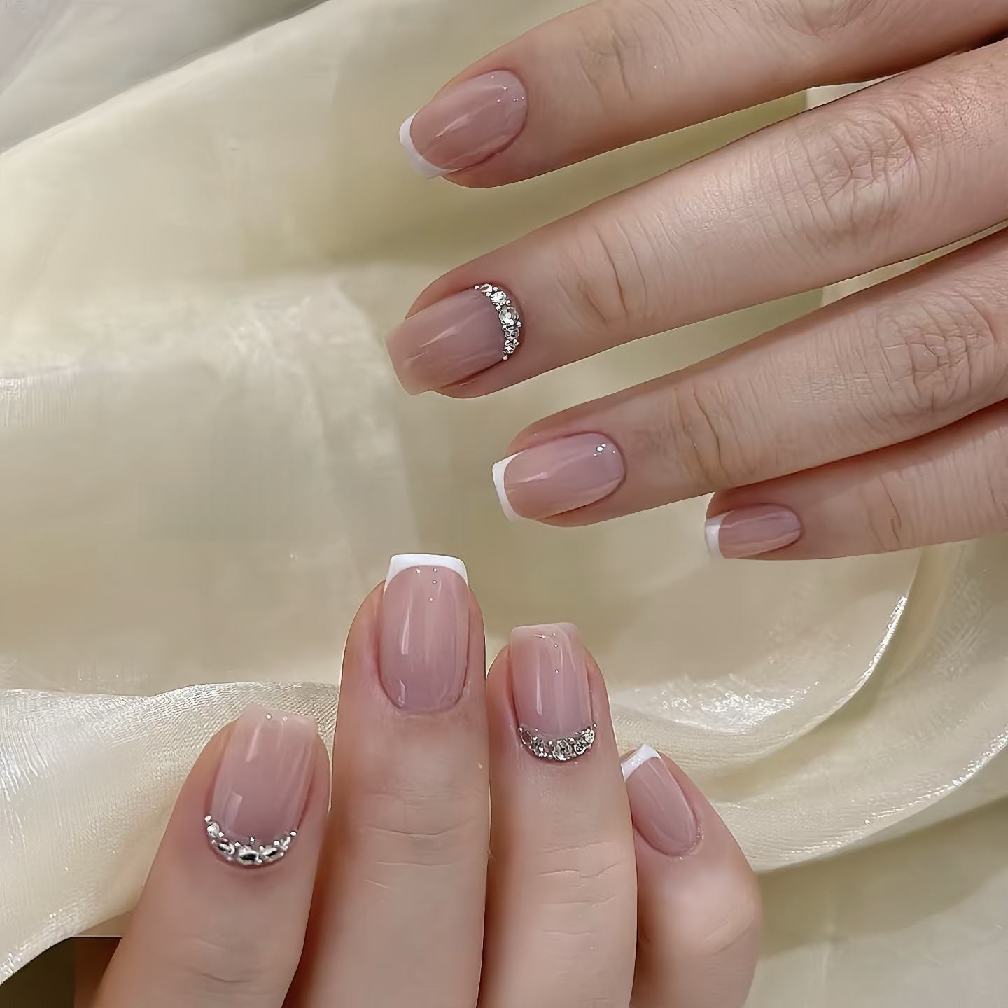 Close-up of hands with pink nail polish and decorative elements on a light fabric background