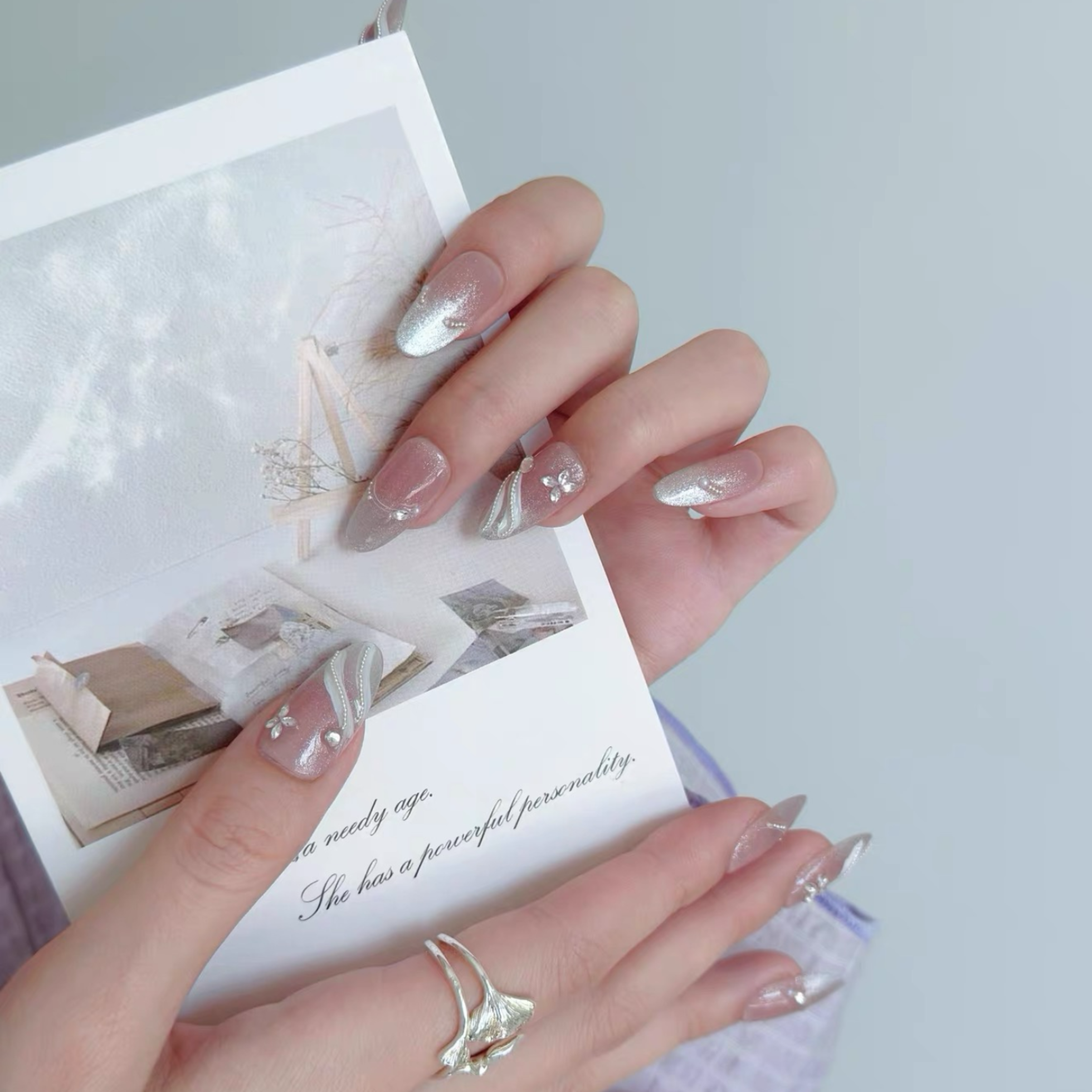 Close-up of hands with silver nail art holding a card with text.