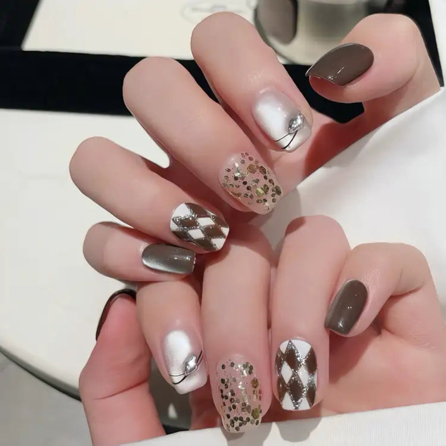 Hand with stylish nail art featuring brown, white, and gold designs.