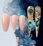 Decorative nail tips with gold and green gemstones on a textured blue and white background